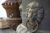 Fototapeta  - A lion head with a ring in its mouth as a decoration on an iron vase against the other vases.