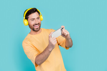 Canvas Print - Photo of young funny freelancer guy makes money in gaming mobile apps watching videos wear headphones isolated on cyan color background