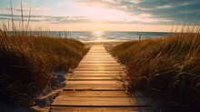  A Wooden Walkway Leading To The Beach With The Sun Setting In The Distance Behind The Grass And The Ocean In The Distance.