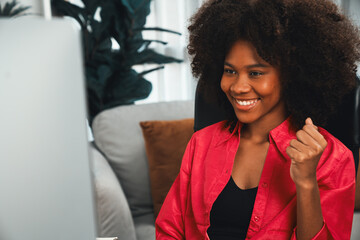 Wall Mural - African woman blogger exited with happy face, looking on screen with valued stock market achievement at high profit. Concept of exchange investment online in trading application on pc. Tastemaker.