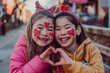 Two cheerful young girls with heart face paint and cute headbands form a heart with their hands, enjoying Valentine's Day