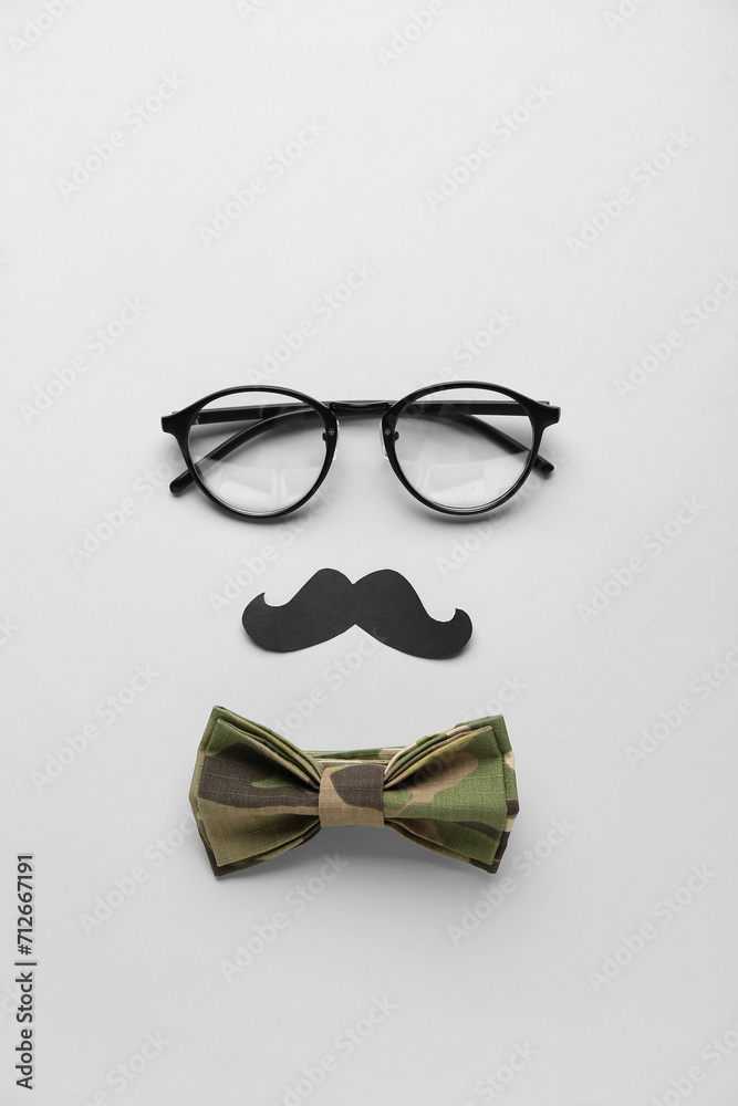 Composition with eyeglasses, paper mustache and bow tie on white background