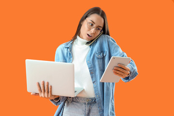 Sticker - Female seller with laptop and tablet computer talking by mobile phone on orange background