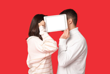 Wall Mural - Young couple with tablet computer on red background. Online dating