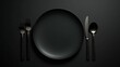 An empty black plate with black cutlery on a noble black table, photographed from above, food photography