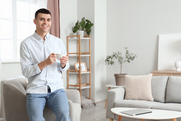 Sticker - Young man with cup of coffee sitting on armchair at home