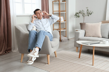 Wall Mural - Young man with headphones listening to music in armchair at home