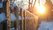 A Close Up Of A Wooden Fence With Snow On The Top Of It And The Sun Shining Through The Trees In The Background.     