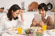 Teenage boy using tablet computer and his upset mother at table during dinner in kitchen. Family problem concept