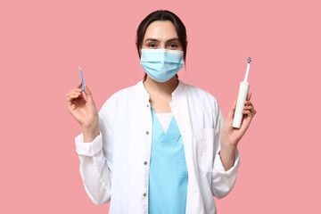 Canvas Print - Young female dentist in mask with electric toothbrush and brush for cleaning braces on pink background