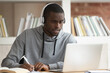 Concentrated biracial male student in Bluetooth headphones look at laptop make notes taking online training distant course, focused african American guy in earphones study watching webinar on computer