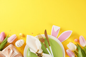 Wall Mural - Easter dining table inspiration. Top view shot of plates, cutlery, napkin, bunnies ears, eggs, gift box, tulips and sprinkles on yellow background with empty space for greeting message