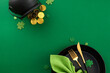 Welcoming St. Patrick's Day at the table. Top view shot of plates, cutlery, green napkin, pot with coins, present, clovers on green background with promo zone