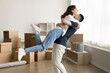© fizkes - Positive excited young couple in love having fun at relocation party, hugging at stacked paper containers, cardboard boxes in background. Strong husband lifting cheerful laughing wife up in air