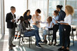 © fizkes - Young diverse ethnic business team and female leader talk chat at office space relax at break share ideas on project in work. Multiethnic staff members engaged in workshop training exchange opinions