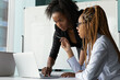 © fizkes - I have question. Black woman teacher stand by desk of mixed race female student look on pc screen help to solve problem. Skilled biracial team leader check online work result of young lady apprentice