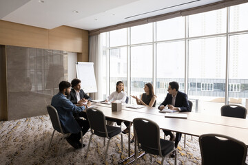 Wall Mural - Positive multiethnic team of project managers talking at large table. Business colleagues brainstorming on plan, strategy on meeting with leader. Partners discussing collaboration. Wide shot