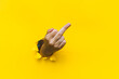 Middle finger of right hand, insulting gesture. Torn hole in yellow paper. Fuck you concept. Aggressive reaction.