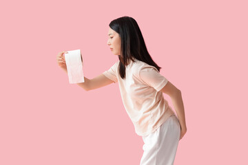 Wall Mural - Young Asian woman with hemorrhoids and toilet paper on pink background