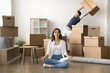 © fizkes - Peaceful calm homeowner woman meditating on floor among moving containers, stressed angry husband leaning under heavy box in background. Married couple going through stressful relocation