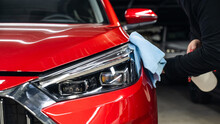 A Man Washes The Headlights Of A Red Car Using A Microfiber Cloth And Spray. 