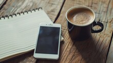 Black coffee in a ceramic mug next to a smartphone and open lined notebook on a textured wooden table, capturing a modern morning routine.
