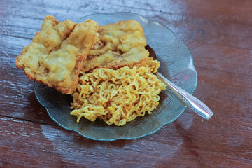 photo of a breakfast dish that is on the table with a menu of fried noodles with 2 fried tempeh and served in a glass plate