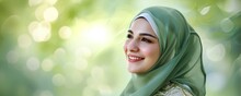 Side View Portrait Of Young Beautiful Asian Muslim Woman Wearing Hijab Looking Away And Smiling While Standing Against Green Background