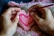 Hands are embroidering a pink heart shape