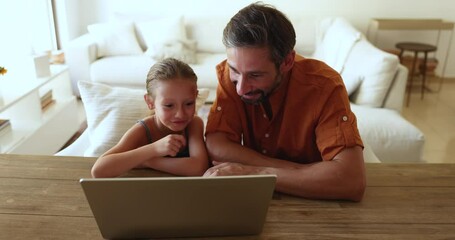 Dad teach little 6s daughter to use laptop, sit at desk staring at computer screen, discuss purchase, watch videos spend time on internet. Modern tech usage for fun, gain new knowledge and development