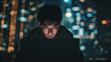 Man focused on laptop with city lights.