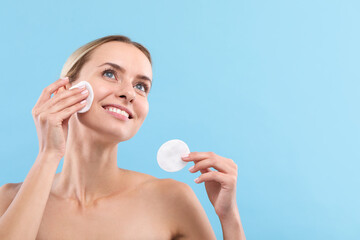 Wall Mural - Smiling woman removing makeup with cotton pads on light blue background. Space for text