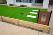 Landscaping project of artificial grass or synthetic turf with a wooden raised garden bed, stepping stones and a mailbox in a front yard outside an Australian residential suburban home.  Copy space