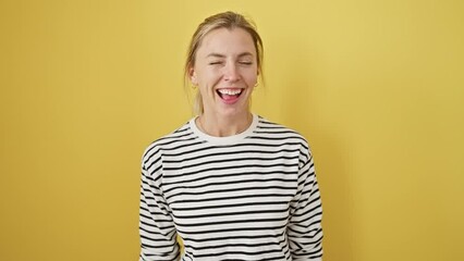 Canvas Print - Jovial young blonde woman, standing isolated against a yellow background, laughing out loud, flashing her smile. can't contain the fun burst out from a crazy hard joke. pure joy personified!