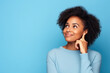 Cute African American lady thinking about her inspiration touch chin looking mockup choosing product option isolated on blue color background