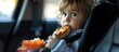 The child is fastened with a seat belt in a car seat and eats a French bun with a sausage A snack in the car during the trip It s a long road A hungry child Car travel. Copy space image