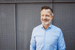 © contrastwerkstatt - Successful Bestager Businessman in Blue Shirt Laughing, Standing confidently against Metal Wall.