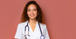 Junge Frau mit langen, lockigen Haaren im Arztkittel und ein Stethoskop umgehängt auf dunkelrosa Hintergrund, copy space