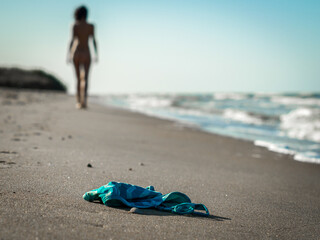 Wall Mural - swimsuit in the sand on the beach near the sea surf on the background of a naked female figure and blue sky