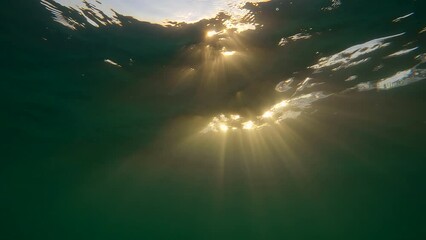 Wall Mural - Sunlight underwater at sundown, Close-up, Slow motion. Rays of the setting sun penetrate under surface of the water. Natural underwater background with sun rays at sunset time