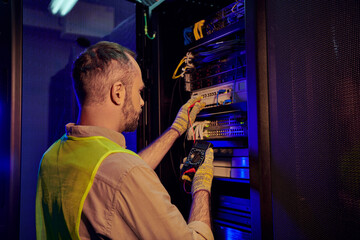 Wall Mural - handsome devoted technician in safety vest and gloves inspecting data center with detector