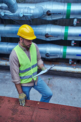 Wall Mural - attractive focused specialist in safety vest and helmet looking at clipboard outside of data center