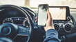 Teen drive a car and use smartphone. Young man reading messages holding a cell phone while driving. Dangerous behavior, accident risk. Danger, transgression, youth, distraction concept. Focus on hand.
