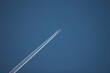 Photo of airplane flying diagonally in the clear blue sky, leaving vapor trail in the air.