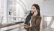 © dodotone - Asian business single woman using smart phone talking holding coffee cup in the city