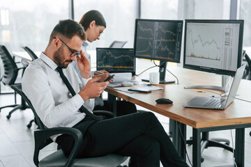 Man is using smartphone. Two employees are working in the office together