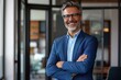 © kimly - Happy middle aged business man ceo standing in office arms crossed. Smiling mature confident professional executive manager, proud lawyer, businessman leader wearing blue suit.