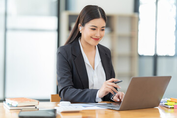 Shot of a young professional woman sitting at desk in front of laptop and using mobile phone working on business contract.