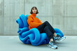 Fashion model with orange knitted sweater and baggy trousers sits on a futuristic looking inflatable chair - Generative AI