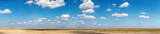 Fototapeta Fototapety z naturą - A panoramic view captures the vastness of an African savannah, with a clear blue sky punctuated by soft clouds, highlighting the natural beauty of the landscape.
